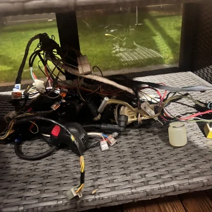 Bok - En hög med olika kablar och ledningar, troligen från ett fordon eller elektronisk utrustning. Kablarna är av olika färger och tjocklekar, och det finns flera kontakter och kopplingar synliga. Perfekt för den som behöver reservdelar eller planerar ett projekt som involverar elektronik.