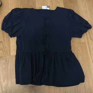 Gullig mörkblå topp från Gina Tricot - Säljer en gullig mörkblå topp från Gina Tricot med korta ärmar och knytning framtill i storlek 170. Toppen har en lös passform och en volangdetalj vid nederkanten och puffärmar. Perfekt för en avslappnad stil!💕💕använd en gång och ser ut som ny!💗💗priset går att diskuteras💓💓💓💋