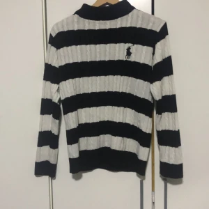 Randig tröja från Ralph Lauren - Snygg svartvit randig tröja från Ralph Lauren med kabelstickat mönster. Tröjan har långa ärmar och en klassisk passform. Perfekt för en stilren look.