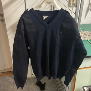 Mörkblå tröja med v-ringning - Säljer en mörkblå tröja med v-ringning och långa ärmar. Tröjan har en enkel design med ribbade muddar vid ärmslut och nederkant. Perfekt för en avslappnad stil.