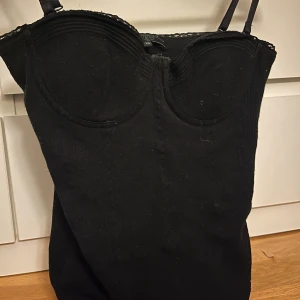 Svart korsett från Guess - Snygg svart korsett från Guess med spetsdetaljer och justerbara axelband. Perfekt för en stilren look.