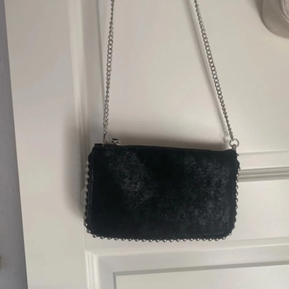 Snygg svart axelväska med kedja och dragkedja. Perfekt för en kväll ute eller en dag på stan. Väskan har en stilren design och är lätt att matcha med olika outfits.. Laukut & Käsilaukut.