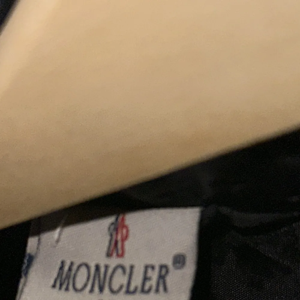 Snygg svart dunväst från Moncler med glansig finish och dragkedja framtill. Västen har Monclers ikoniska logotyp på bröstet och är perfekt för kyligare dagar.. Takit.