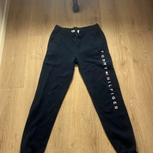 Marinblå mjukisbyxor från Tommy Hilfiger - Säljer ett par marinblå mjukisbyxor från Tommy Hilfiger med logotyp längs benet. Byxorna har en elastisk midja och är perfekta för en avslappnad stil. Tillverkade i mjukt material för extra komfort. Står att de passar i åldrar mellan 16-18 men tycker själv att de sitter som S