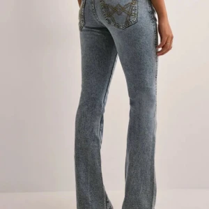 Blå twisted bootcut jeans med broderade detaljer - Snygga blå twisted bootcut jeans med broderade detaljer på bakfickorna. Perfekta för en avslappnad stil med en touch av unik design. De har en klassisk femficksmodell och är lågmidjade. Säljer dessa då jag tyckte de va för lågmidjade och inte passa min kroppsform. Orginalpris 499kr knappt använda, lägger ut de för 300kr pris kan diskuteras!