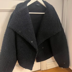 Svart teddyjacka från Gina Tricot - Mysig svart teddyjacka från Gina Tricot med en oversized passform. Jackan har stora slag och knappar framtill, perfekt för kyliga dagar.