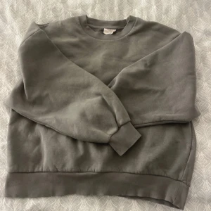 Mörkgrön/grå sweatshirt - Säljer en bekväm grå sweatshirt med rund hals och långa ärmar. Perfekt för en avslappnad stil. Passar bra till jeans eller mjukisbyxor. Storlek L men passar allt därunder. Jag har vanligtvis xxs/xs