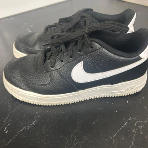 Svarta Nike Air Force sneakers - Snygga svarta Nike Air Force sneakers med vit sula och vit swoosh. Skorna har klassisk snörning. 