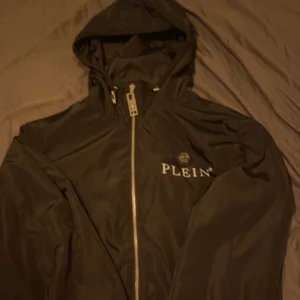 Svart vindjacka från Philipp Plein - Snygg svart vindjacka från Philipp Plein med huva och dragkedja framtill. Perfekt för blåsiga dagar och har en stilren design med logotyp på bröstet. Storlek S men passar M. Den är köpt i Spanien, kvitto samt påse kommer med.