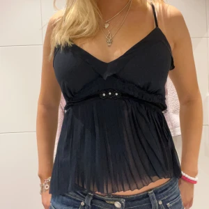 Festtopp - Snygg svart ärmlös topp med v-ringning och plisserad nederdel. Toppen har smala axelband och en dekorativ detalj i midjan.😊