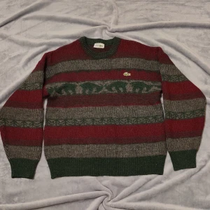 Randig stickad tröja från Lacoste - Säljer en snygg stickad tröja från Lacoste i randigt mönster med gröna, röda och grå nyanser. Tröjan har långa ärmar och det klassiska Lacoste-märket på bröstet. Perfekt för kyligare dagar! Storlek 4 Chemise Lacoste, made in France Använd och tvättad Har varit väl omhändertagen  Inget defekt eller hål på tröjan    #stitchedsweater #lacoste #christmasthemed #woolsweater #akryl #vintage #vintagestyle #chemiselacoste #mediumsize #medium #darkred #darkgreen #gray #warm #stitched #sweater