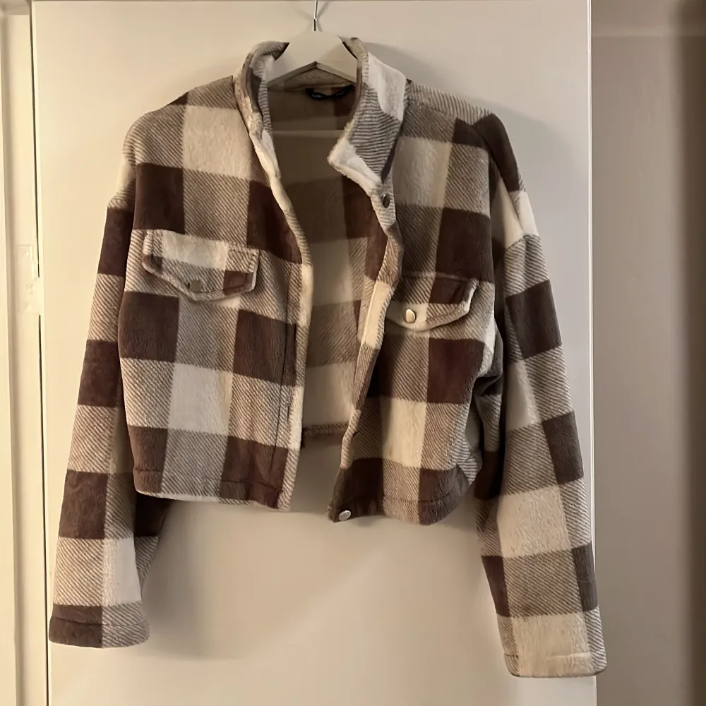 Säljer en brun, vit grön rutig jacka med knappar och två bröstfickor. Jackan är croppad och är supermjuk och mysig!😍. Takit.