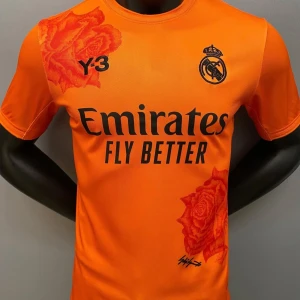 Orange fotbollströja från Y-3 - Snygg orange fotbollströja från Y-3 med Real Madrid-logga och Emirates Fly Better-tryck. Tröjan har korta ärmar och coola rosdetaljer i samma färg. Perfekt för fotbollsfans som vill sticka ut på planen!