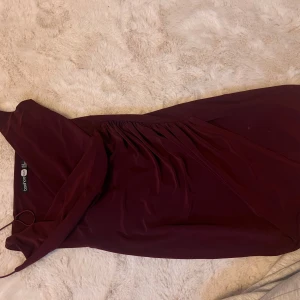 Vinröd klänning från Boohoo - Elegant vinröd klänning från Boohoo med omlott-design och v-ringad hals. Perfekt för en stilren look.
