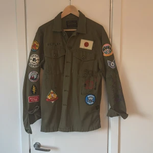 Grön overshirt med patches från Replay - Säljer en grön overshirt från Replay med coola patches över hela jackan. Den har långa ärmar och knappar framtill. Perfekt för en unik och avslappnad stil. Nypris 1300 kr, Mitt pris 800. Används 2 gånger och är köpt från replay hede fashion outlet.