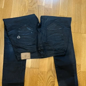 Svarta jeans med slitningar  - Snygga svarta jeans med coola slitningar och en liten hjärtdetalj på bakfickan. Perfekta för en avslappnad stil. De har en klassisk femficksdesign och knappgylf. Den är i nyskick
