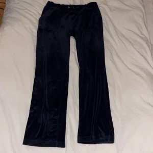 Marinblåa juicy couture byxor med snörning - Snygga marinblåa juicy couture byxor i mjukt material med snörning i midjan. Byxorna har fickor med knappar baktill och en avslappnad passform. Perfekta för en bekväm och stilren look. Ena snöret har åkt in i hålet men finns att ta fram.