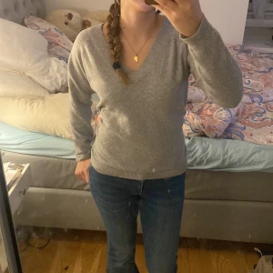 Grå v-ringad tröja - Säljer en stilren grå v-ringad tröja med långa ärmar. Perfekt för kyligare dagar och lätt att matcha med olika outfits.