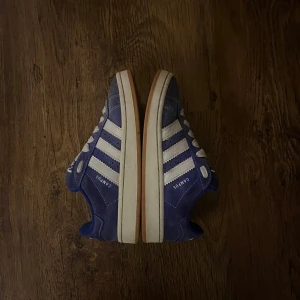 Blå Adidas Campus sneakers - Snygga blå Adidas Campus sneakers med vita detaljer och klassiska tre ränder på sidan. Skorna har en bekväm passform och snörning framtill. De är använda men i jättebra skick. Om ni vill ha fler bilder på skorna så får ni gärna skriva till mig!nypris är 1250kr 💙