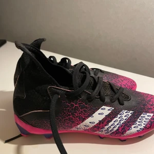 Adidas Predator fotbollsskor strl 34  - Snygga Adidas Predator fotbollsskor i svart och rosa med. Skorna har en iögonfallande design med rosa detaljer och mönster på ovansidan. Perfekta för fotbollsplanen. Bra skick använda ett fåtal gånger 