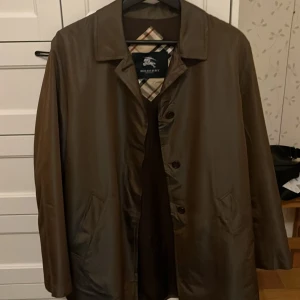 Brun trenchcoat från Burberry - Elegant brun vintage trenchcoat från Burberry med klassiskt rutigt foder. Jackan har knappar framtill och två fickor. Perfekt för höst och vår. Skriv gärna vid fler frågor!