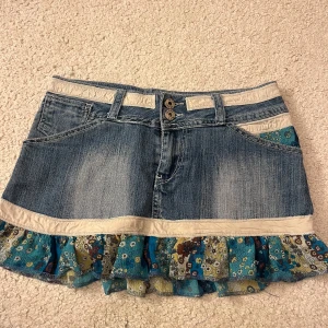 Jeanskjol med volang från My Industry - Snygg jeanskjol från My Industry med volangdetalj i blått och blommigt mönster. Kjolen har knappar fram och fickor både fram och bak. Midjemått: 37cm rakt över. Längd: 28 cm. Använd gärna köp nu 💕💕