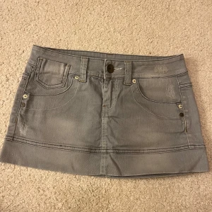 Grå jeanskjol från Benetton - Snygg grå jeanskjol från Benetton med klassisk femficksdesign och knappstängning. Snygg detalj baktill! Midjemått: 37 cm rakt över. Längd: 27cm. Använd gärna köp nu💕💕