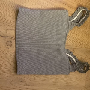 Grå ribbad topp med volangdetaljer jag vet inte vilken butik eller storlek det är men jag skulle säga 12-13 - Snygg grå ribbad topp med volangdetaljer på axelbanden. Perfekt för en stilren och trendig look. Toppen är ärmlös och har en bekväm passform.