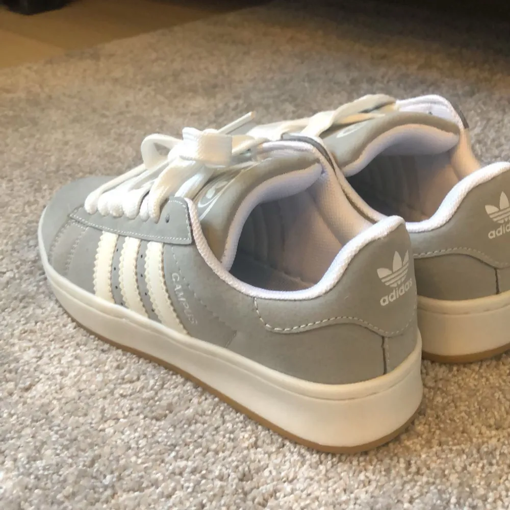 Säljer ett par snygga gråa Adidas Campus sneakers i mycket bra skick. De har den klassiska tre-randiga designen i vitt på sidan och är perfekta för vardagsbruk. Skorna är bekväma och stilrena, med en mjuk sula för extra komfort. Perfekta för både vår och höst! Har använt dom ett få tal gånger!. Skor.