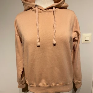 Aprikos färgad hoodie från Lager 157 M - Säljer en supermysig Aprikos hoodie från 157 i storlek M. Det står XS i hoodien men det är mer en M. Perfekt för höst och vinter med sin mjuka insida och klassiska design. Den har en justerbar huva med dragsko och ribbade muddar vid ärmslut och nederkant. Passar perfekt för en avslappnad stil! 🍂