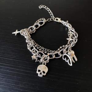 Coolt silverfärgat armband med flera kedjor och unika berlocker som en dödskalle, stjärnor, vingar och en tand. ca 16 cm och kan justeras upp till 20 cm! Perfekt för att ge din outfit en edgy touch. Armbandet har en justerbar kedja för att passa olika storlekar. Passar perfekt till både vardag och fest!