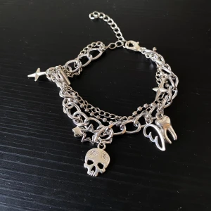 Handgjort Silverfärgat armband med berlocker - Coolt silverfärgat armband med flera kedjor och unika berlocker som en dödskalle, stjärnor, vingar och en tand. ca 16 cm och kan justeras upp till 20 cm! Perfekt för att ge din outfit en edgy touch. Armbandet har en justerbar kedja för att passa olika storlekar. Passar perfekt till både vardag och fest!