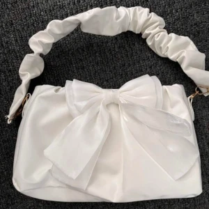 Vit axelväska med rosett - Superfin vit axelväska i syntetmaterial med en stor dekorativ rosett på framsidan. Väskan har ett unikt handtag med rynkade detaljer som ger den en extra touch. Perfekt för att piffa upp en outfit till fest eller vardag. 👜✨köpt för 800 säljer för 380 (helt oanvänd) 