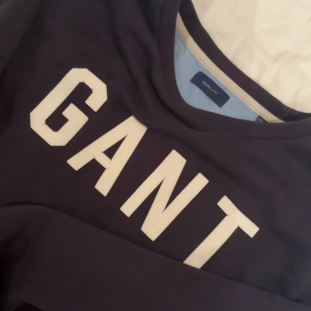 Säljer en snygg mörkblå sweatshirt från GANT i mycket bra skick. Den har en klassisk design med GANT-loggan i vitt på bröstet. Perfekt för en avslappnad stil och passar till både jeans och joggers. Superbekväm och stilren!. Tröjor & Koftor.