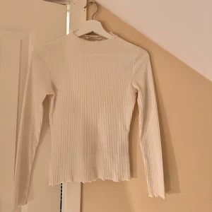 Vit ribbad tröja - Säljer en stilren vit ribbad tröja med långärmad design. Perfekt för både vardag och festliga tillfällen. Tröjan har en skön passform och är gjord i ett mjukt material som känns bekvämt mot huden. Ett måste i garderoben för alla säsonger!