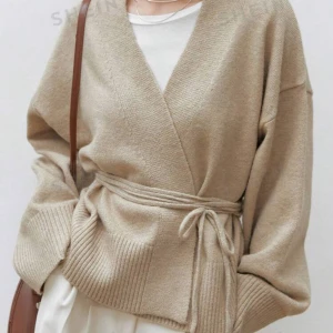 Beige stickad kofta med knytband - Superfin beige stickad kofta som är perfekt för höst och vår. Den har en omlott-design med ett knytband i midjan som ger en snygg passform. Långärmad och ribbad vid ärmslut och nederkant. Perfekt att slänga på sig för en mysig och stilren look!