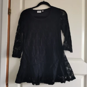 Svart spetsklänning från Amalia - Snygg svart klänning från Amalia i spetsmaterial. Den har trekvartsärmar och en elegant passform som passar perfekt för festliga tillfällen. Klänningen är i bra skick och har en fin detalj med spetsmönster över hela plagget.