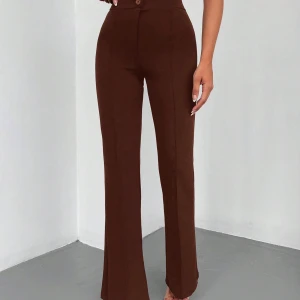 Bruna kostymbyxor - Snygga bruna kostymbyxor i högmidjad modell. De har en elegant bootcut-stil som ger en fin siluett. Perfekta för både kontoret och festligare tillfällen. Byxorna har en klassisk design med knappar framtill.