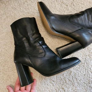 KIOMI Svarta stövletter med klack - Snygga svarta stövletter från KIOMI med en stabil klack och dragkedja på sidan. Perfekta för höst och vinter, dessa boots har en stilren design med en fyrkantig tå. De är i mycket bra skick och passar både till vardags och fest.