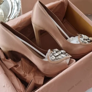 Eleganta pumps från Miu Miu - Säljer ett par superchica pumps från Miu Miu i nude av satin. De har en hög klack och är dekorerade med glittriga stenar i ett hjärtmönster på tån. Perfekta för en fest eller en speciell kväll. Skorna är i nytt skick och kommer i originalförpackning. Använda en enda gång. Extra klackar medföljer.