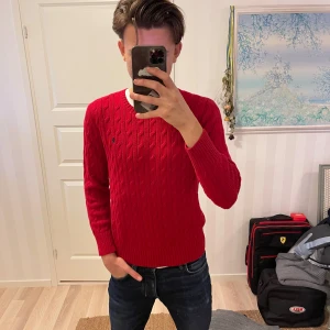 Röd kabelstickad tröja från Polo Ralph Lauren - Säljer en snygg röd kabelstickad tröja från Polo Ralph Lauren. Den har en klassisk design med rund hals och det ikoniska logotypbroderiet på bröstet. Perfekt för både höst och vinter, och den är i mycket bra skick. Passar perfekt till jeans för en stilren look! Är L i ungdomstorlek men passar Xs/ och kanske S i vuxenstorlek med fantastiskt skick! 
