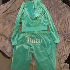 Säljer en supermjuk och snygg grön velour hoodie och matchande byxor från Juicy Couture. Hoodien har dragkedja och glittrig text på bröstet, medan byxorna har samma glittriga text på baksidan. Perfekt för en chill dag hemma eller en avslappnad utflykt. 🧃✨Byxorna har ett super litet hår tyvärr, syns dock nästan inte alls när dom är på! Tröjan är i storlek XS, byxorna är i storlek S. 