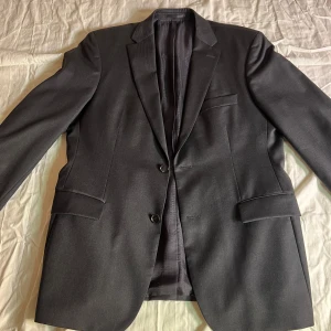 Grå kavaj från BOSS - Säljer en elegant grå kavaj från BOSS i Super 100 ull. Kavajen har en klassisk design med två knappar och fickor fram. Perfekt för både formella och semi-formella tillfällen. Passar bra till höst och vår. Jag är 190 och kavajen är lite för stor, skulle rekommendera den om du kanske är i samma längd men lite mer bredaxlad och kanske väger runt 90
