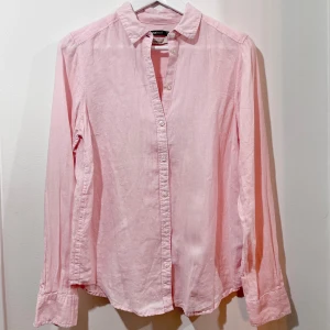 Ljusrosa linneskjorta - Säljer en superfin ljusrosa skjorta i linne. Den har en klassisk krage och knappar hela vägen ner. Perfekt för både vardag och fest! Skjortan är långärmad och har en avslappnad passform. Passar perfekt till jeans eller kjol för en chic look. 100% linne.