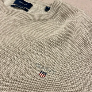 Beige stickad tröja från GANT - Säljer en  beige stickad tröja från GANT i storlek S. Tröjan är gjord av premium bomull och har en liten broderad logga på bröstet. 