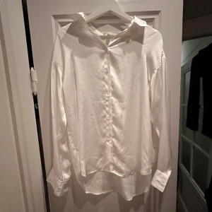 Vit satinskjorta - Säljer en klassisk vit långärmad satinskjorta. Skjortan har en stilren design. Perfekt för både vardag och festliga tillfällen. Passar bra till jeans eller kostymbyxor för en mer uppklädd look. Skrynklig pga legat i påse på vinden
