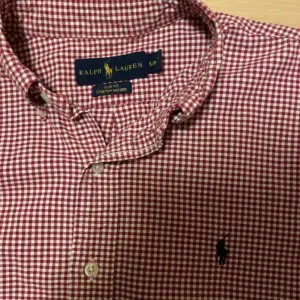 Säljer en snygg röd och vit rutig skjorta från Ralph Lauren i storlek S. Skjortan är i stretchigt bomullsmaterial och har en klassisk krage med knappar. Den är långärmad och har en broderad logga på bröstet. Perfekt för både vardag och fest!