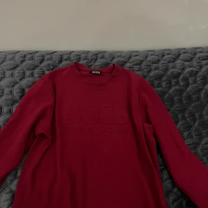 Tröja Hugo Boss - Säljer en snygg röd tröja från Hugo Boss i storlek M. Tröjan är i bra skick och har en stilren design med långärmade ärmar. Perfekt för både höst och vinter. Passar till både vardag och fest! Pris kan diskuteras 