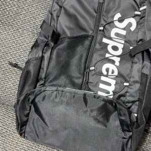Svart ryggsäck från Supreme - Säljer en snygg svart ryggsäck från Supreme. Den har ett stort huvudfack med dragkedja och meshfickor på sidorna. Perfekt för skolan eller vardagsbruk. Den är i mycket bra skick och redo för nya äventyr!