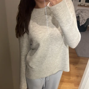 Beige stickad tröja - Mysig grå/vit stickad tröja i mycket bra skick. Perfekt för höst och vinter med sin varma och bekväma design. Tröjan har långa ärmar och en klassisk rund halsringning. 